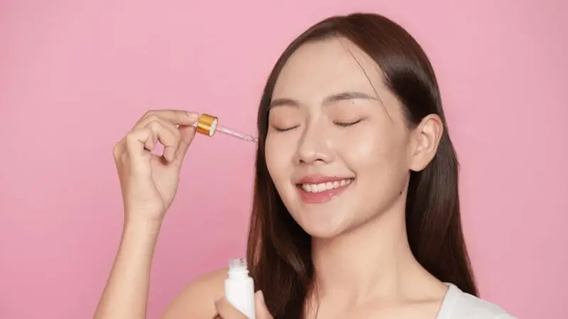 Uśmiechnięta dziewczyna aplikuje serum do twarzy