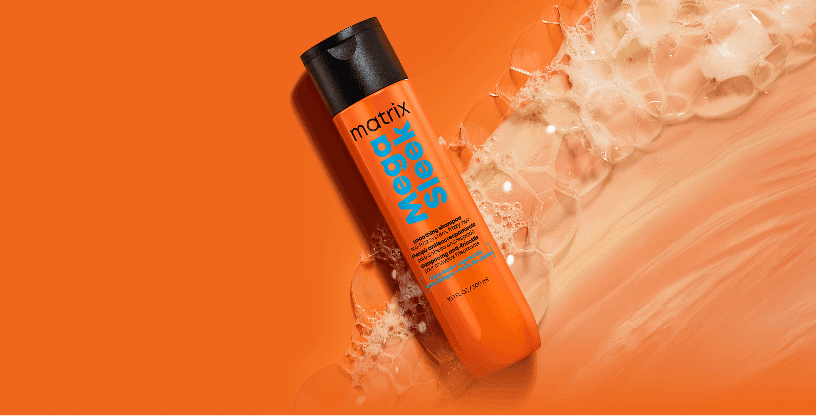 Pomarańczowa butelka szamponu Matrix Mega Sleek otoczona delikatną, lśniącą pianą na jednolitym, pomarańczowym tle.