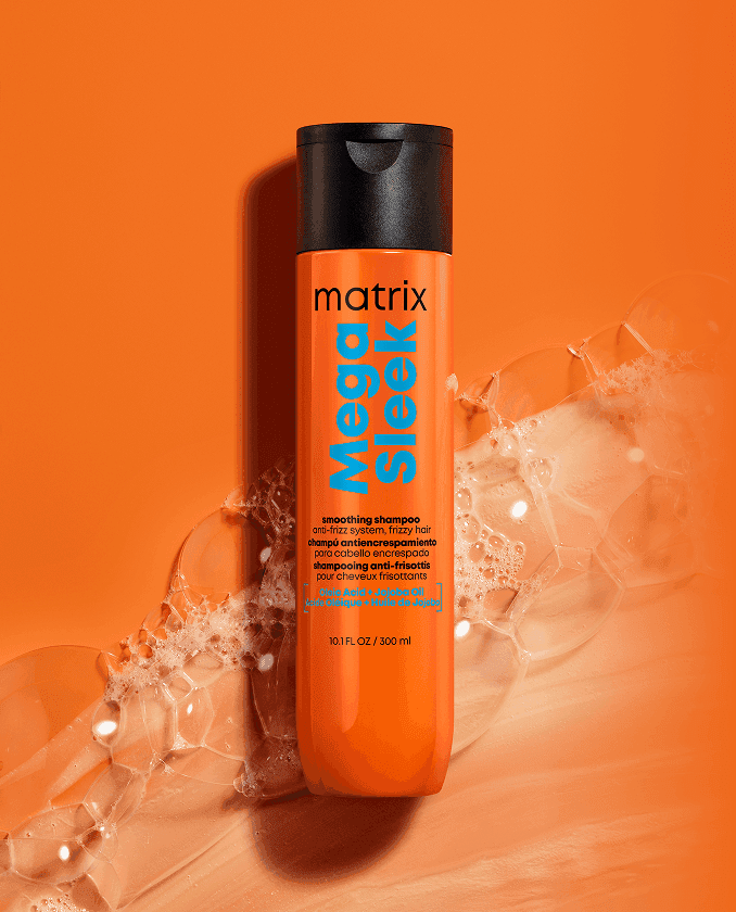 Pomarańczowa butelka szamponu Matrix Mega Sleek otoczona delikatną, lśniącą pianą na jednolitym, pomarańczowym tle.